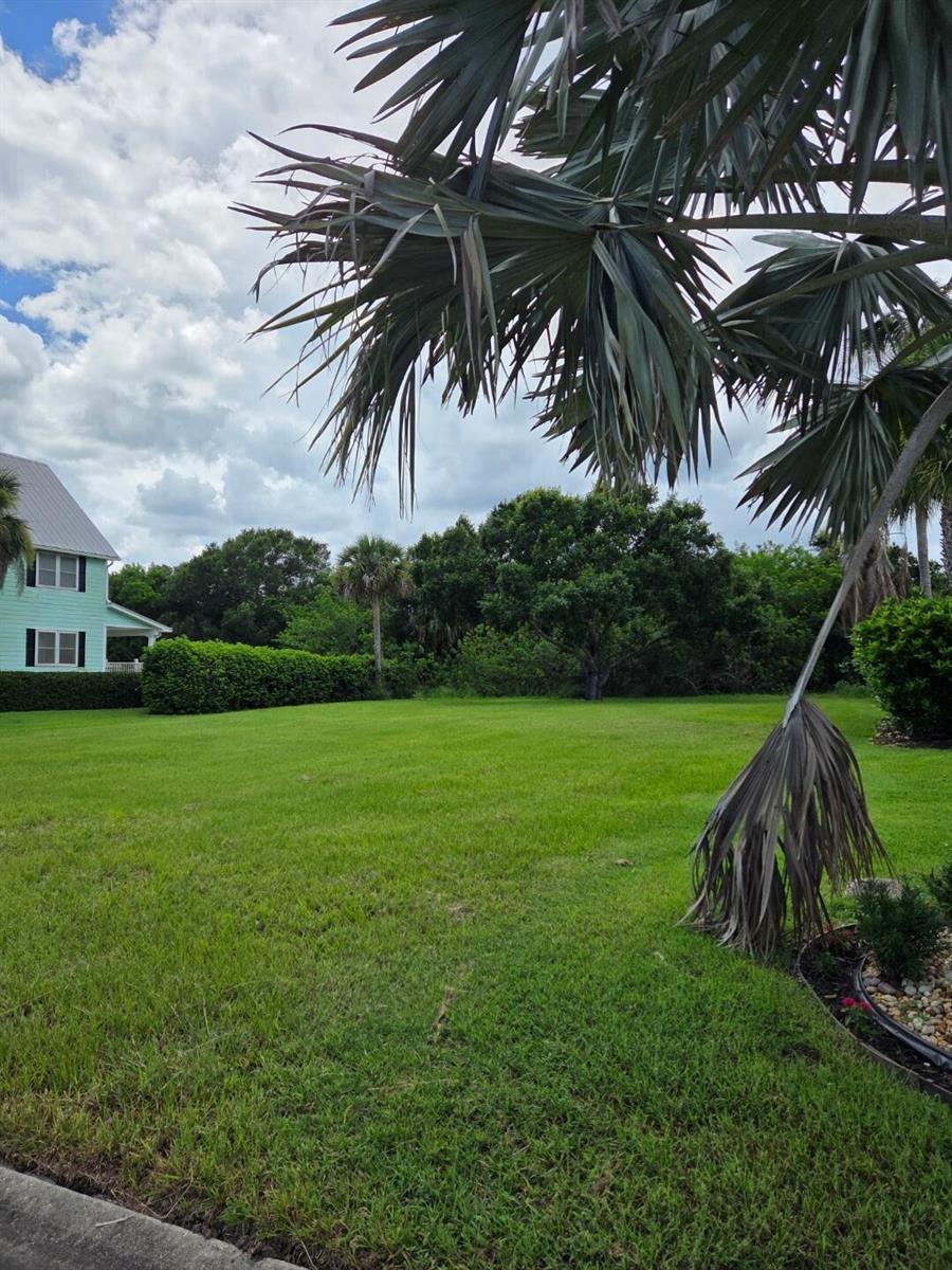 A large green lawn sits in front of a light green house and trees — 6385 Tropical Way, Vero Beach FL 32967, VERO BEACH, FL