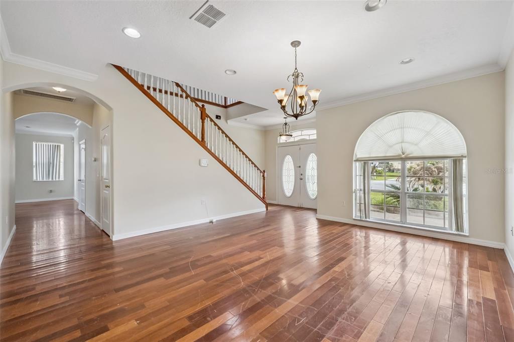 An empty foyer features hardwood floors, a wooden staircase, and a large arched window — 106 CASTLEFORD WAY, KISSIMMEE, FL