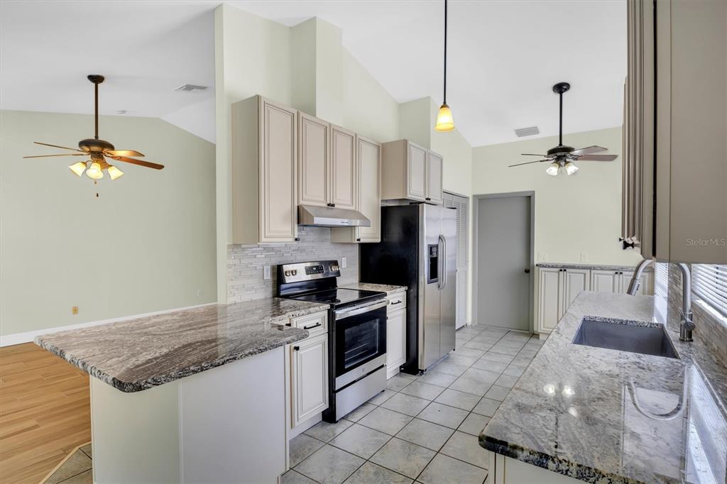 A kitchen features granite countertops, light-colored cabinets, stainless steel appliances, and tile flooring — 3631 102ND PLACE N, CLEARWATER, FL