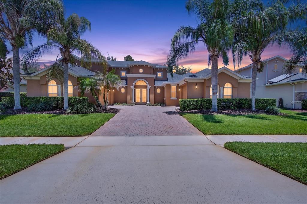 A single-story stucco house with a brick driveway and palm trees at dusk — 3198 HEIRLOOM ROSE PLACE, OVIEDO, FL