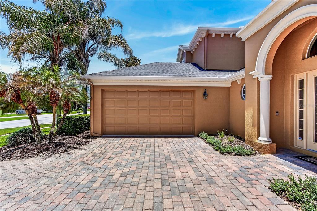 A tan house features a two-car garage, a paver driveway, and palm trees — 3198 HEIRLOOM ROSE PLACE, OVIEDO, FL
