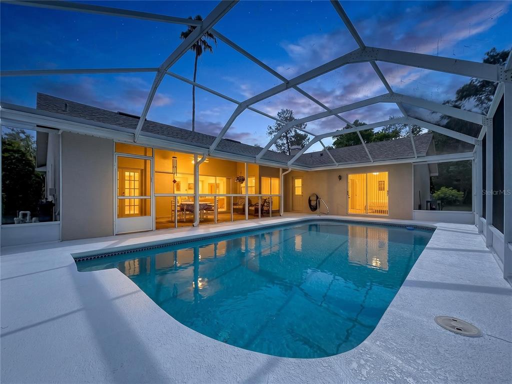 A swimming pool sits inside a screened-in lanai attached to the back of a house — 12380 TANSBORO STREET, SPRING HILL, FL