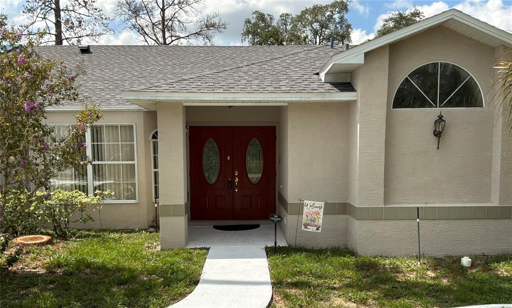 A tan house exterior features a red double front door and a concrete walkway — 12380 TANSBORO STREET, SPRING HILL, FL
