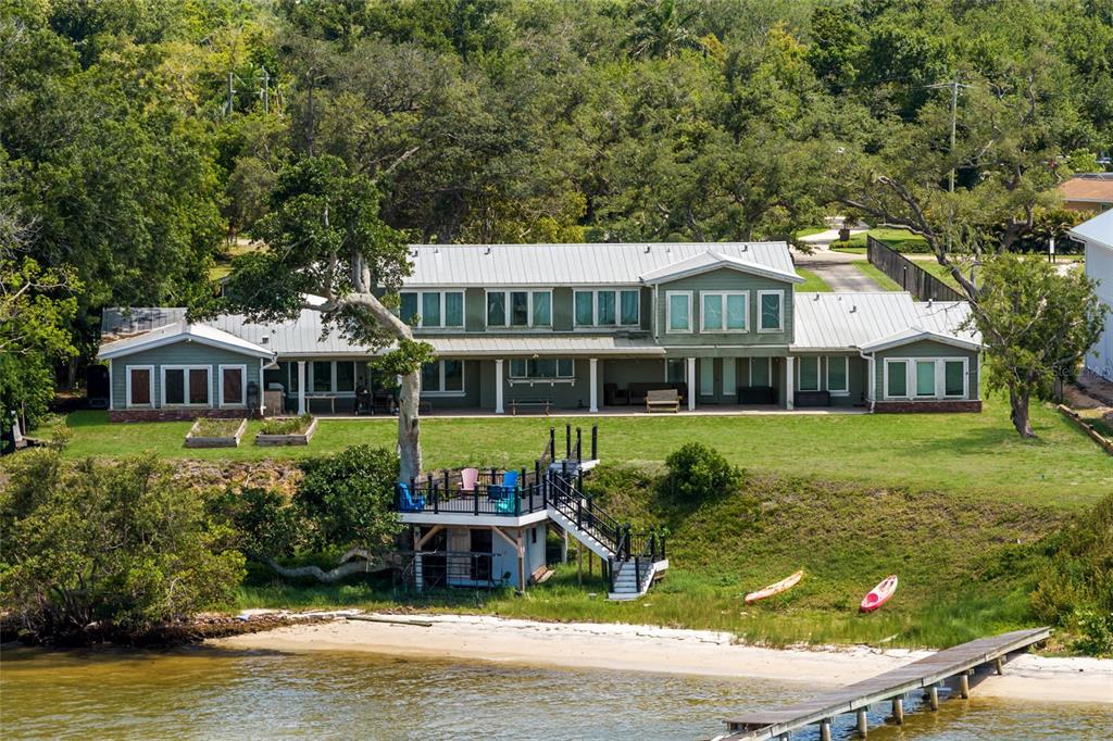 An aerial view of a two-story green house with a metal roof and waterfront deck — 4900 RIVERVIEW BOULEVARD, BRADENTON, FL