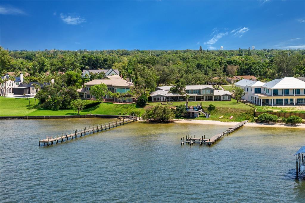 An aerial view shows three waterfront houses with private docks along a grassy shoreline — 4900 RIVERVIEW BOULEVARD, BRADENTON, FL