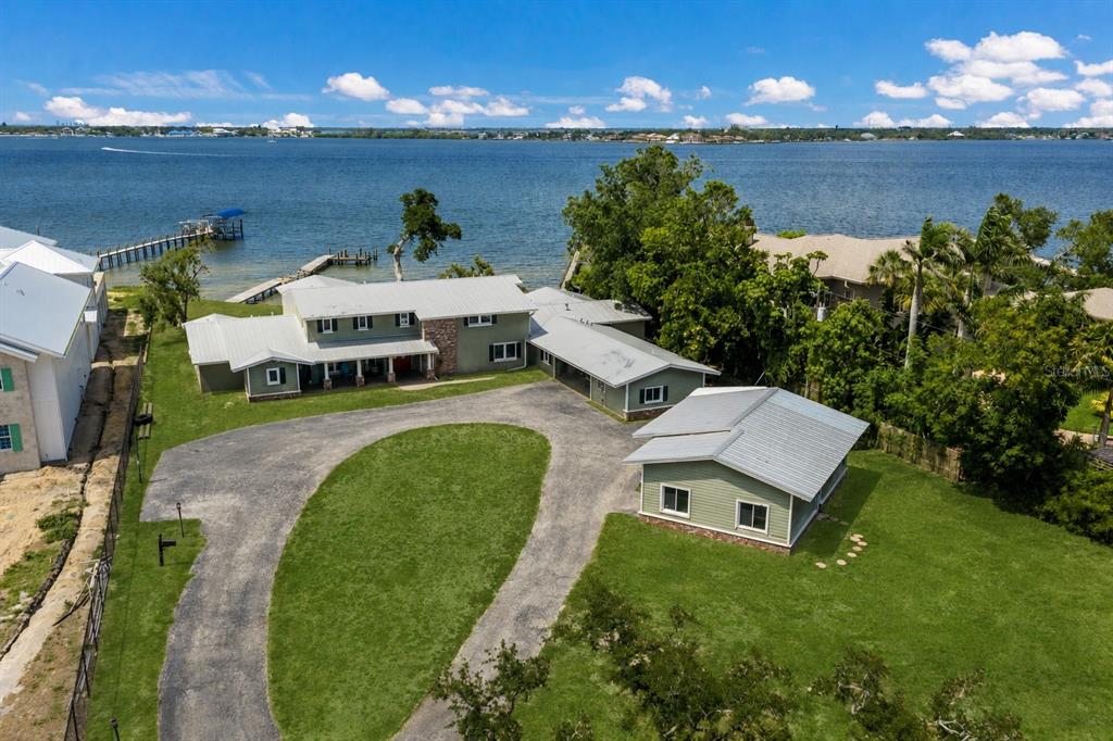 An aerial view shows a green house with a metal roof, circular driveway, and dock — 4900 RIVERVIEW BOULEVARD, BRADENTON, FL