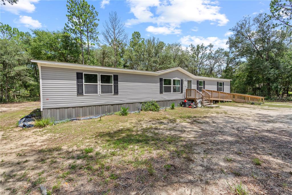 A single-story manufactured home with grey siding and a wooden wheelchair ramp sits on a lot — 8551 NE 102ND COURT, BRONSON, FL