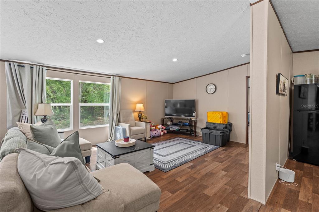 A living room features wood-look flooring, a sectional sofa, a television, and two windows — 8551 NE 102ND COURT, BRONSON, FL