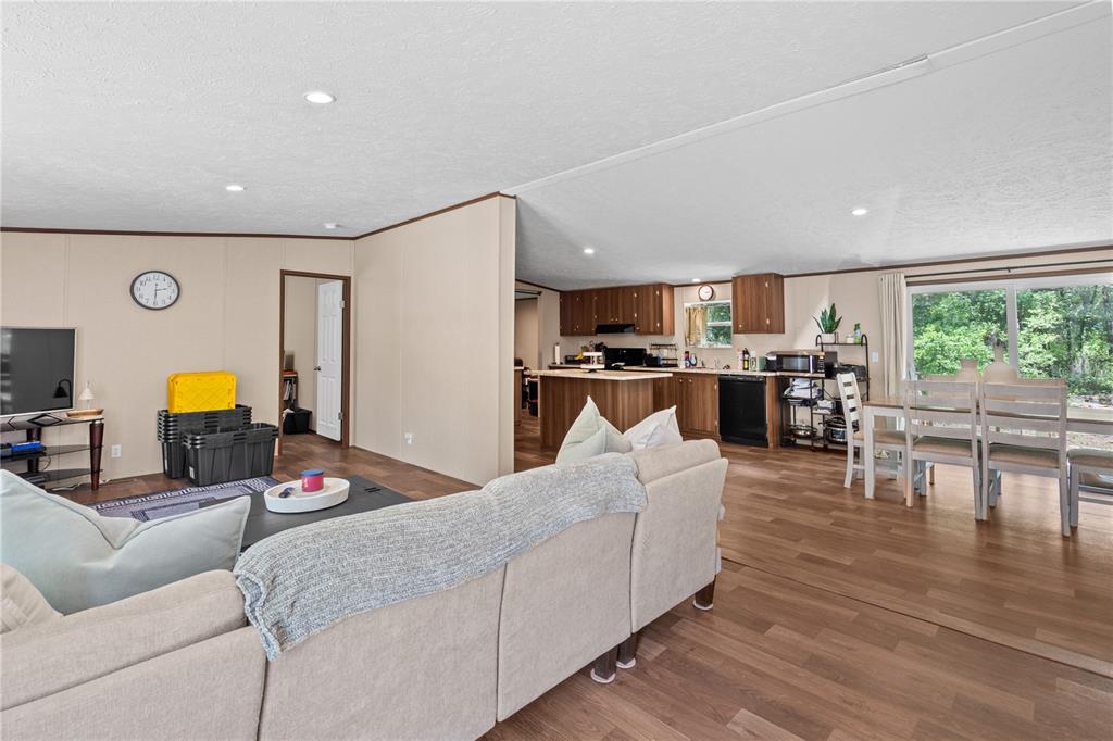 An open-concept living room and kitchen featuring wood-look flooring, beige walls, and a sectional sofa — 8551 NE 102ND COURT, BRONSON, FL