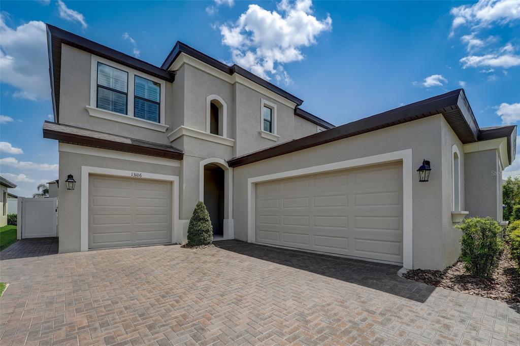 A two-story house with a three-car garage and a paved driveway under a blue sky — 13106 FOXTAIL FERN DRIVE, RIVERVIEW, FL