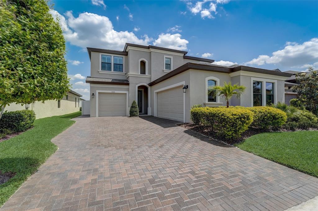 A two-story house with a beige stucco exterior, a brick paver driveway, and two garages — 13106 FOXTAIL FERN DRIVE, RIVERVIEW, FL