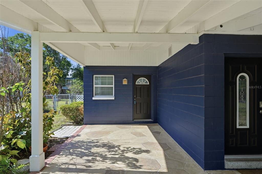A covered patio with stone flooring sits in front of a blue house with two doors — 1708 POND LAKE DRIVE, TAMPA, FL