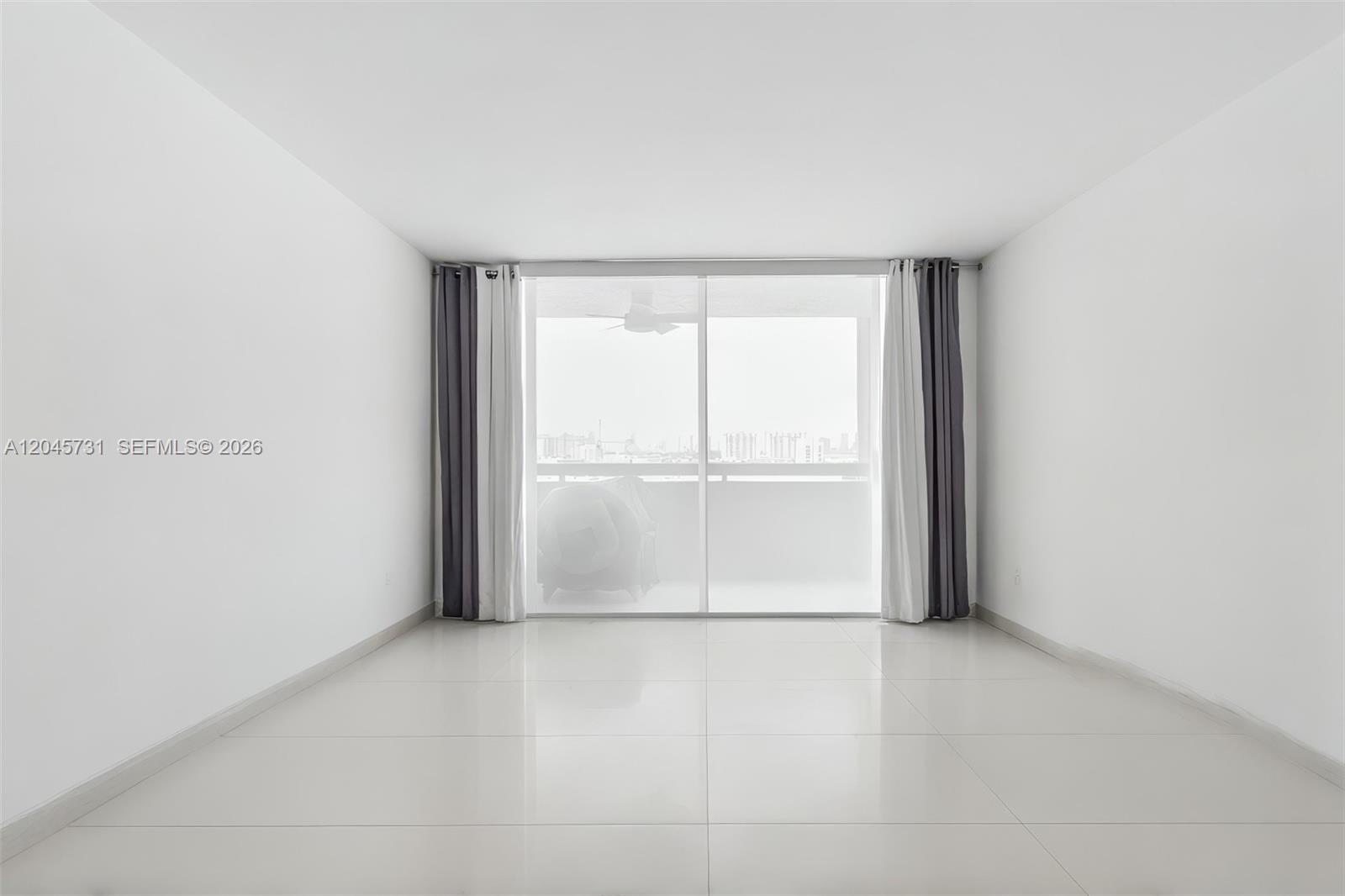 A bright, empty room features white walls, light tile flooring, and a sliding glass balcony door — 1775 Washington Ave # 14F, Miami Beach FL 33139, MIAMI BEACH, FL