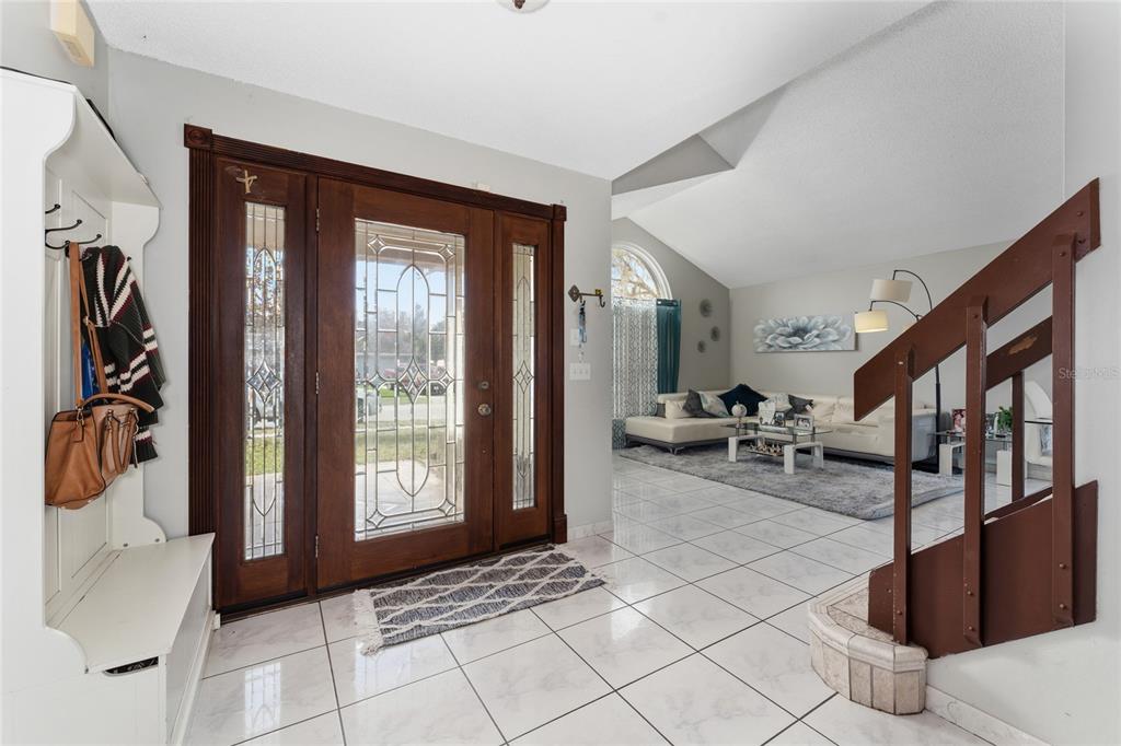 An entryway with white tile floors, a wooden front door, and a staircase with railings — 8713 CATBRIAR BAY WAY, ORLANDO, FL