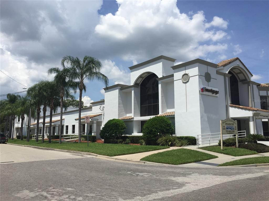 A parking lot with several parked cars, mature trees, and a yellow directional arrow — 2111 W SWANN AVENUE, TAMPA, FL