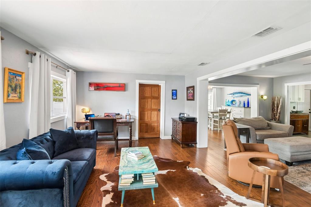 A living room features a blue sofa, a cowhide rug, a wooden desk, and hardwood floors — 992 HILLWOOD DRIVE, DUNEDIN, FL