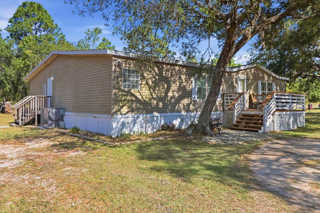 A tan manufactured home with a wooden deck and stairs sits on a grassy lot — 5015 S ORWELL POINT, HOMOSASSA, FL