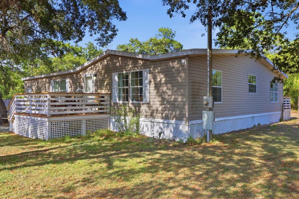 A tan mobile home with a wooden deck and white lattice skirting sits on grass — 5015 S ORWELL POINT, HOMOSASSA, FL