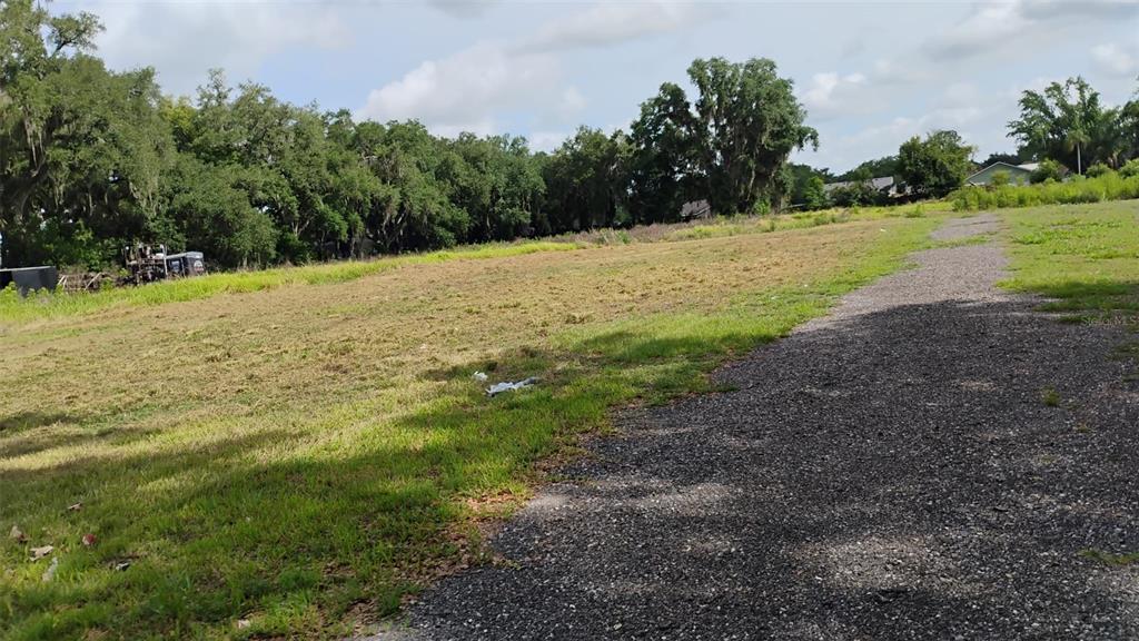A gravel driveway leads through a cleared, grassy lot toward a line of mature trees — PLEASANT ACRE DR, PLANT CITY, FL