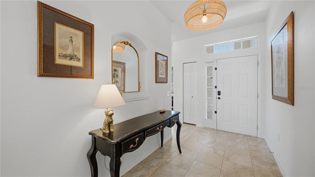 A bright entryway features a dark console table, a lamp, a mirror, and tile flooring — 12630 ROCKROSE GLEN, LAKEWOOD RANCH, FL