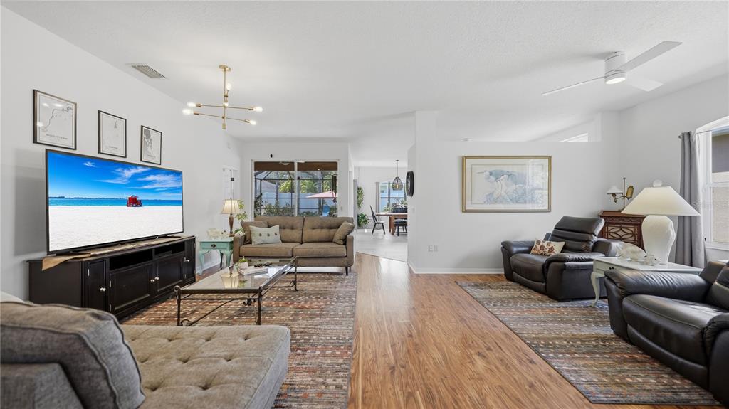 A living room features wood-look flooring, two seating areas, and a large wall-mounted television — 12630 ROCKROSE GLEN, LAKEWOOD RANCH, FL