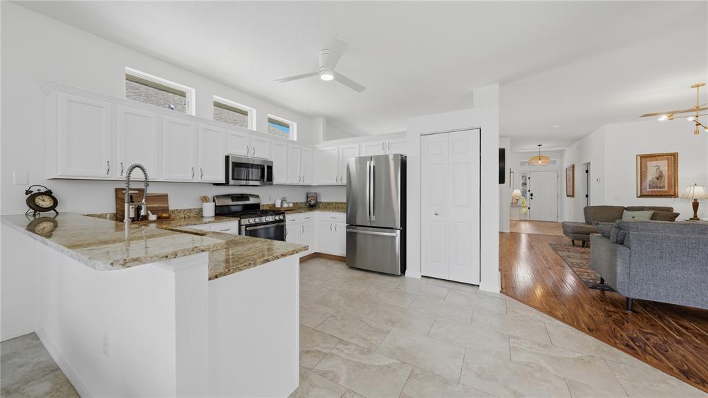 A kitchen with white cabinets, granite countertops, and stainless steel appliances opens to a living area — 12630 ROCKROSE GLEN, LAKEWOOD RANCH, FL