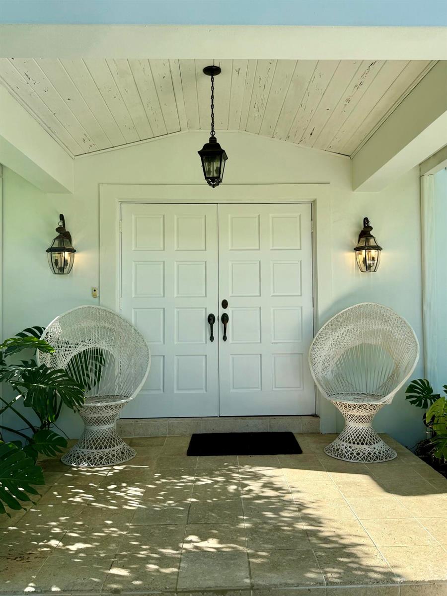 A covered porch features two white wicker chairs flanking a set of double white doors — 222 Miraflores Drive, Palm Beach FL 33480, PALM BEACH, FL