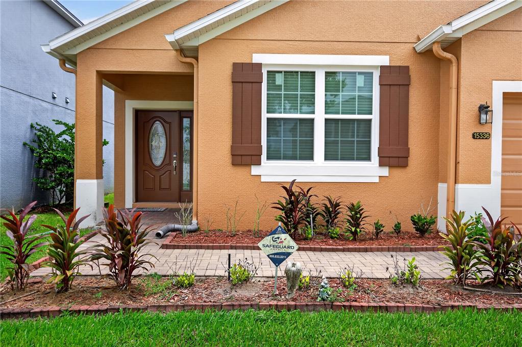 The exterior of a tan house features a front door, a window with shutters, and landscaping — 15336 TREVISO STREET, ORLANDO, FL