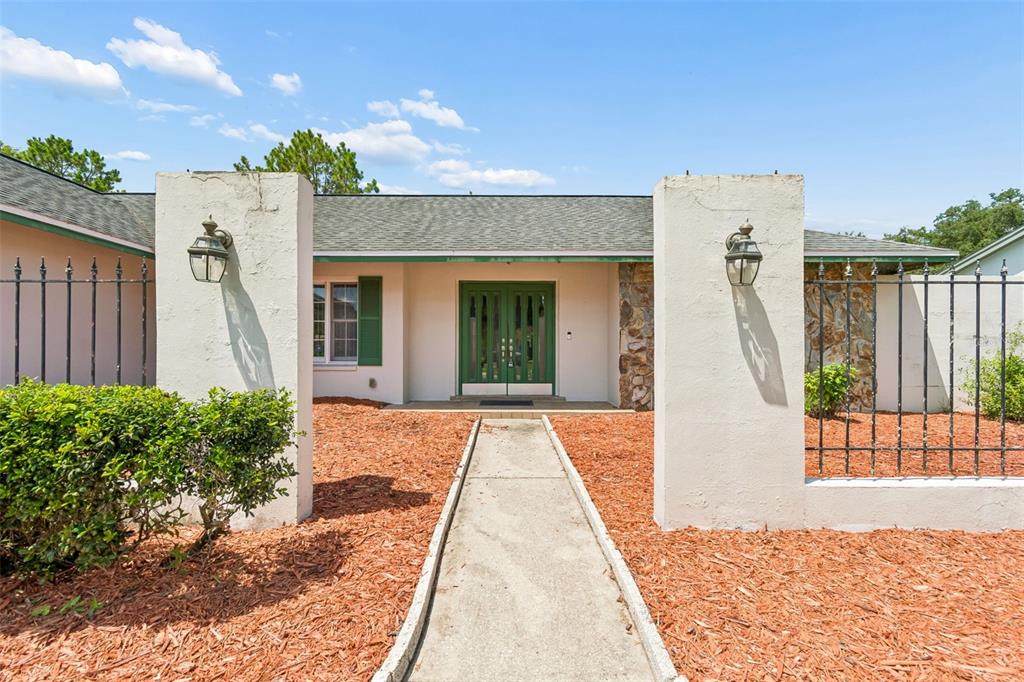 A concrete walkway leads to the green double front doors of a single-story house — 9237 PEBBLE CREEK DRIVE, TAMPA, FL