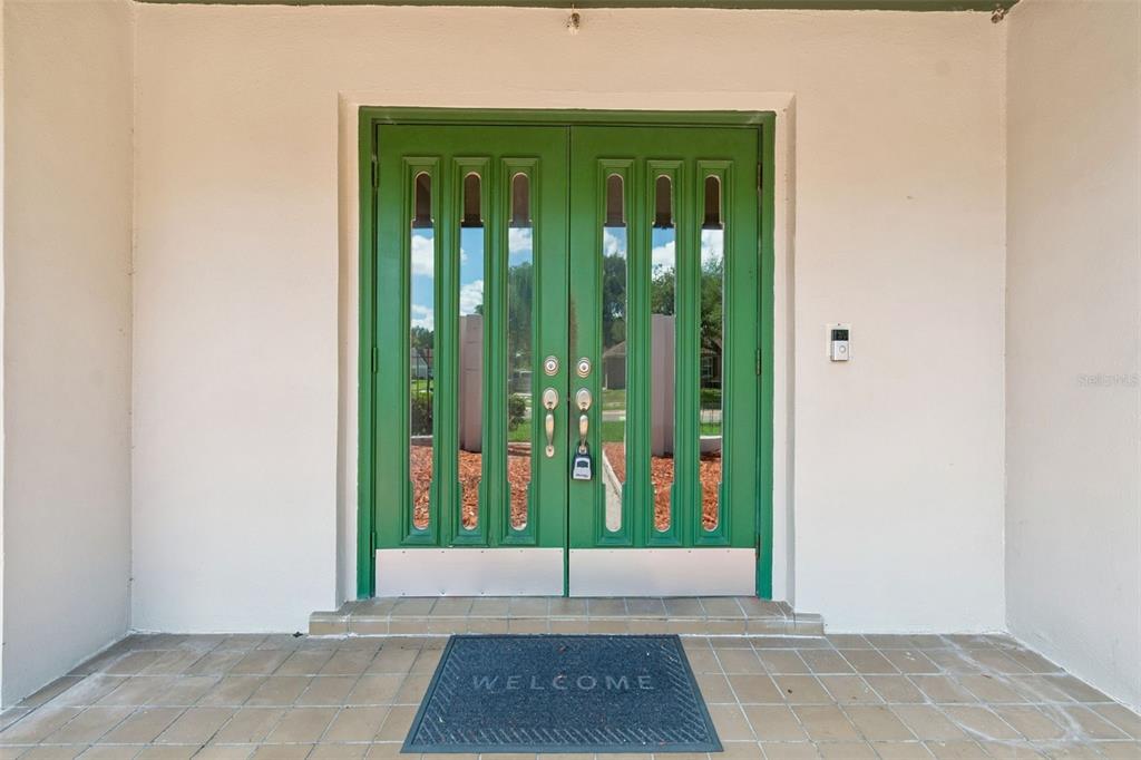 A pair of green double doors with vertical glass panels sits on a tiled porch — 9237 PEBBLE CREEK DRIVE, TAMPA, FL