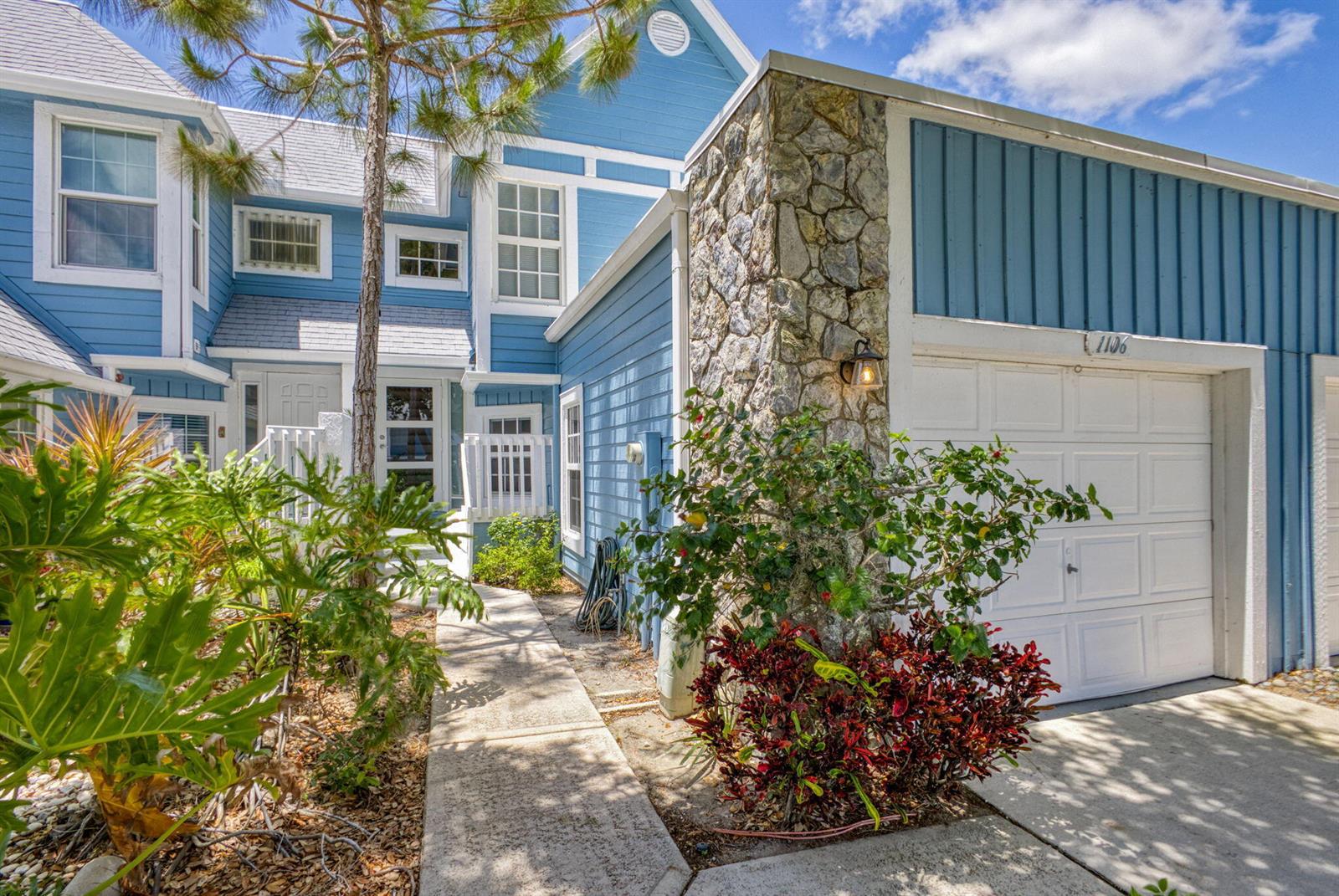A blue two-story house features a stone chimney, a white garage door, and a walkway — 1106 Ocean Dunes Circle, Jupiter FL 33477, JUPITER, FL
