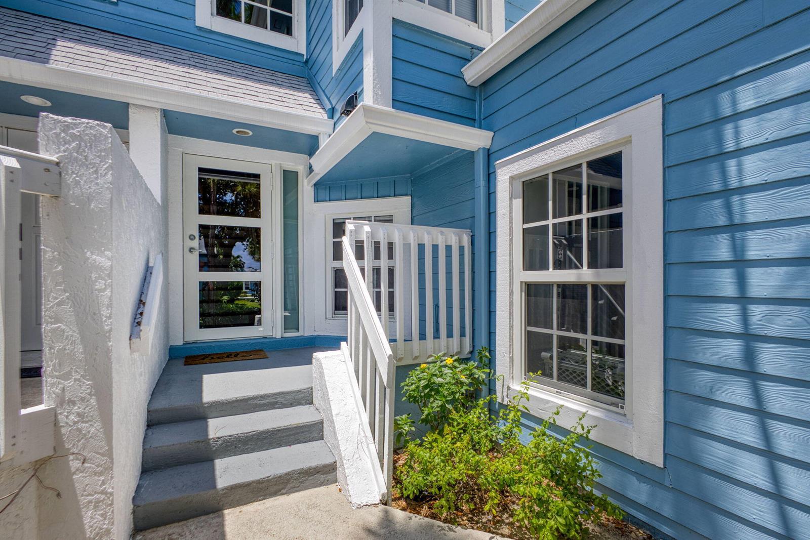 A blue house exterior features a white-trimmed front door, gray steps, and a small garden — 1106 Ocean Dunes Circle, Jupiter FL 33477, JUPITER, FL