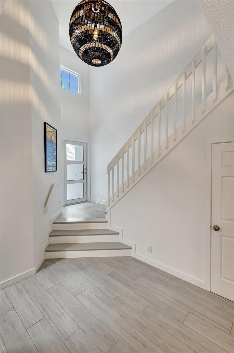 A bright entryway features light wood-look tile floors, a staircase with white railings, and a chandelier — 1106 Ocean Dunes Circle, Jupiter FL 33477, JUPITER, FL