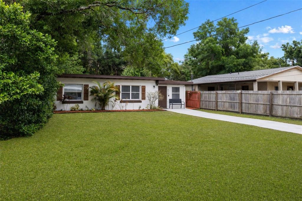 A single-story white house with brown trim features a large front lawn and concrete driveway — 8707 N ASHLEY STREET, TAMPA, FL