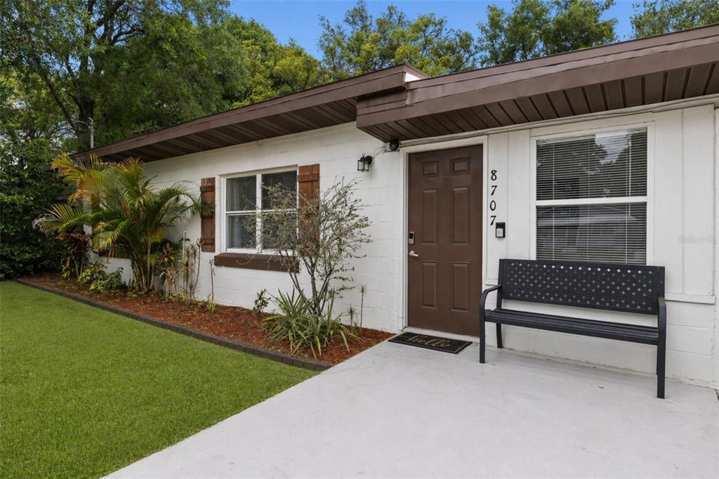 A single-story house exterior features a white block wall, brown door, and a black bench — 8707 N ASHLEY STREET, TAMPA, FL