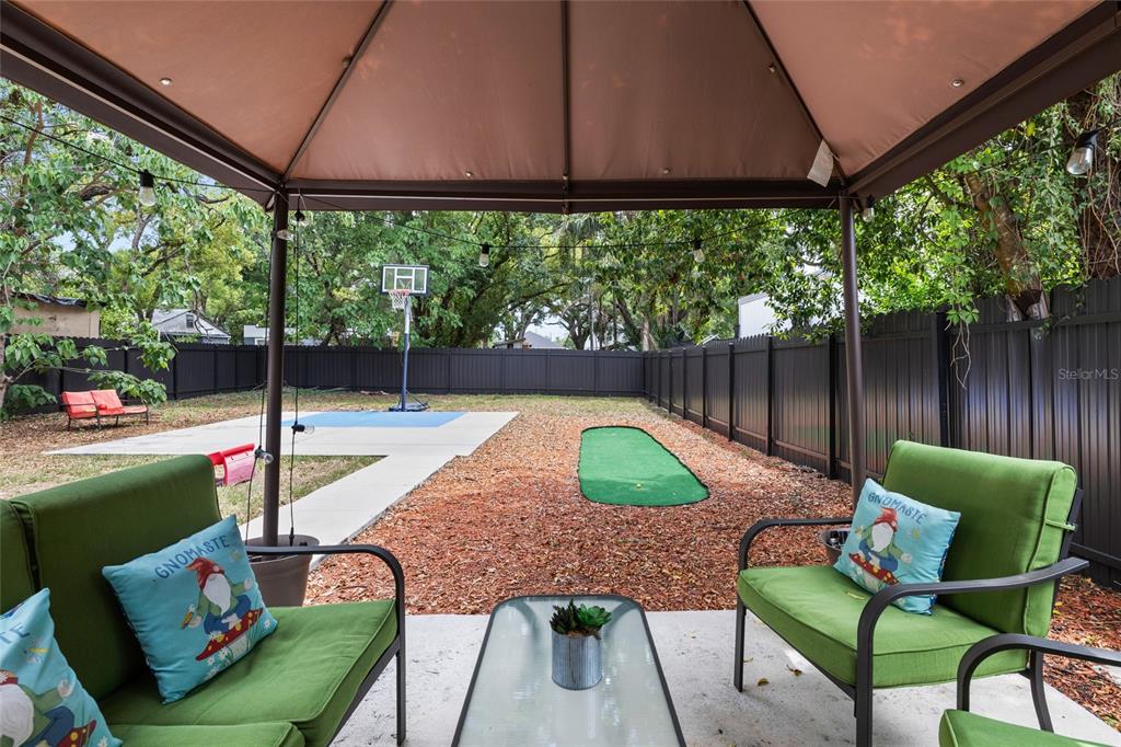 A backyard patio features a gazebo, green chairs, a putting green, and a basketball hoop — 8707 N ASHLEY STREET, TAMPA, FL