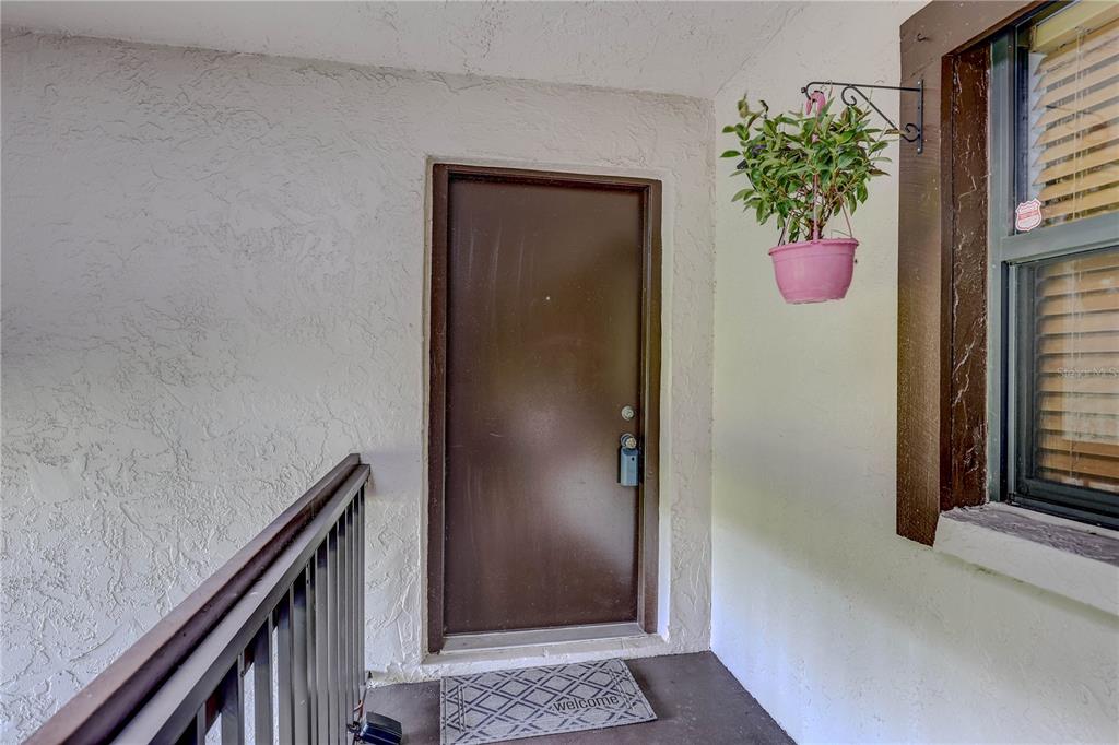 A brown front door is situated on a covered porch next to a window — 2400 WINDING CREEK BOULEVARD UNIT 26-203, CLEARWATER, FL