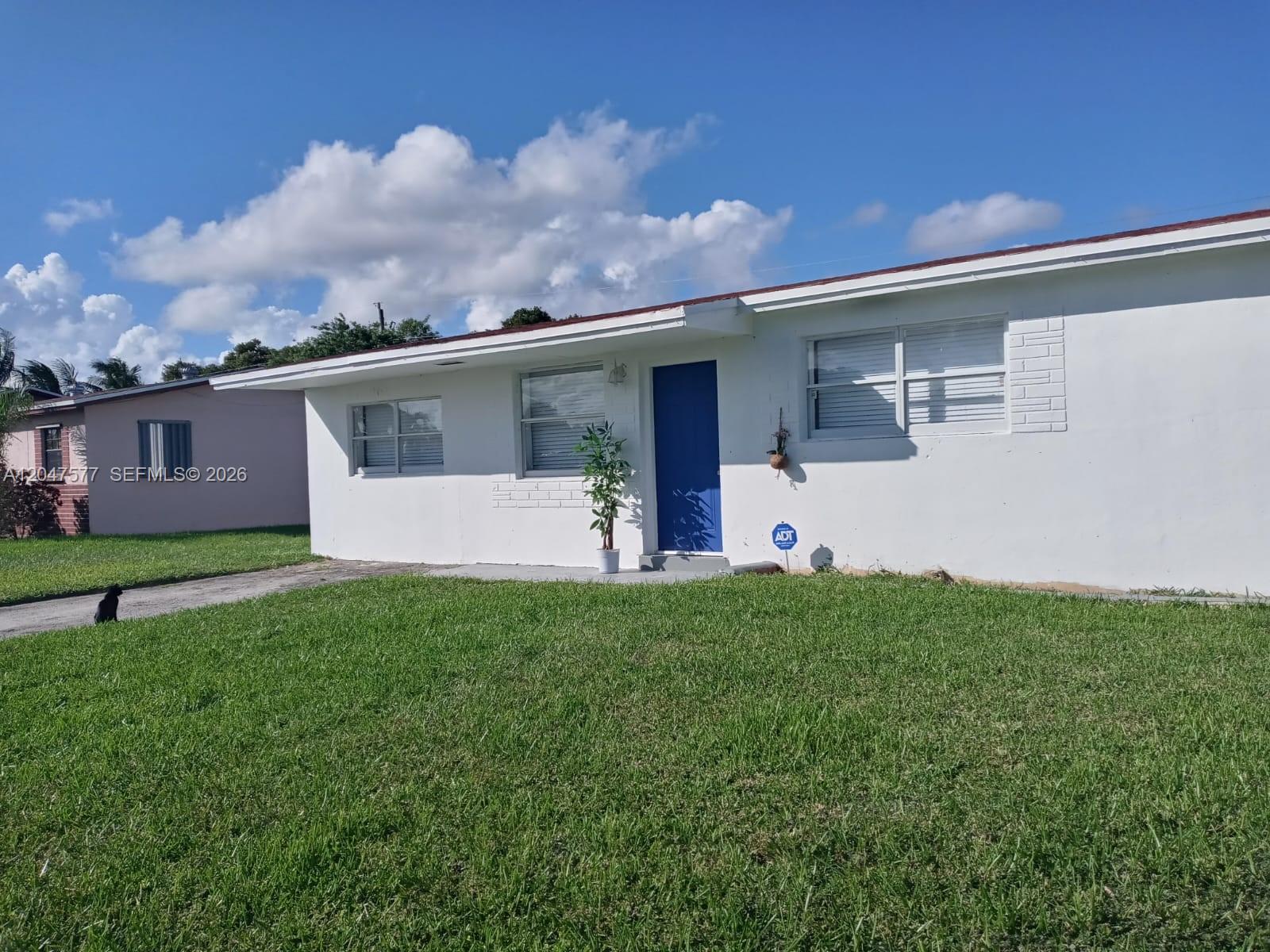 A white single-story house with a blue front door sits behind a green lawn — 10961 SW 222nd Ter, Miami FL 33170, MIAMI, FL