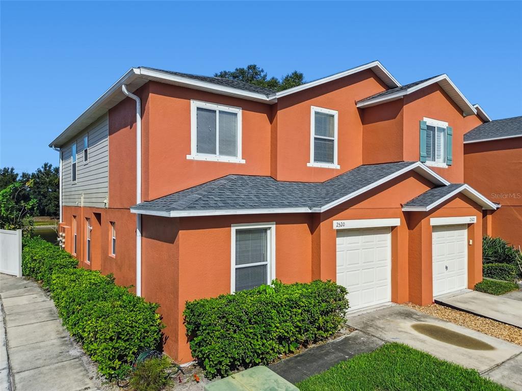 A two-story orange stucco duplex with two garage doors and green hedges in front — 2520 COLONY REED LANE, CLEARWATER, FL