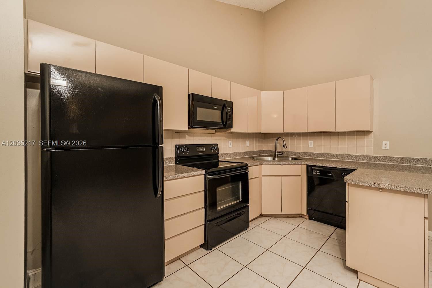 A kitchen features black appliances, beige cabinets, tiled floors, and speckled countertops — BOCA RATON, FL