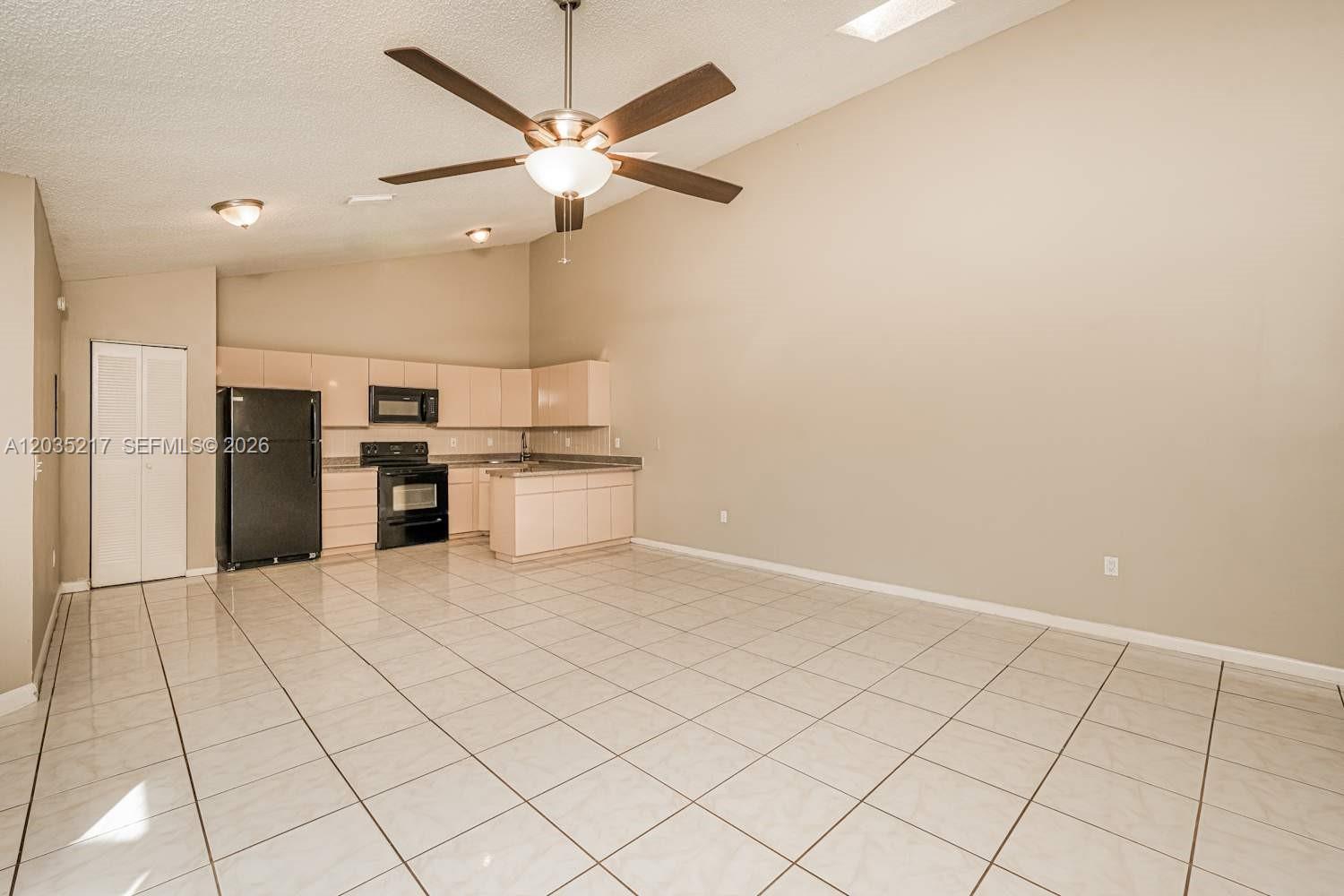 An open-concept kitchen features light-colored cabinets, black appliances, and tile flooring under a vaulted ceiling — BOCA RATON, FL