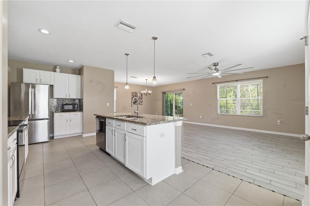 A kitchen with white cabinets and a granite island opens into a spacious living area — 13755 COVEY RUN PLACE, SPRING HILL, FL