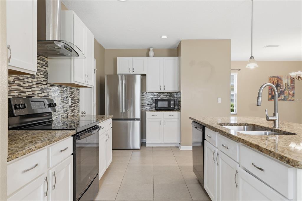A kitchen features white cabinets, granite countertops, stainless steel appliances, and a tiled backsplash — 13755 COVEY RUN PLACE, SPRING HILL, FL