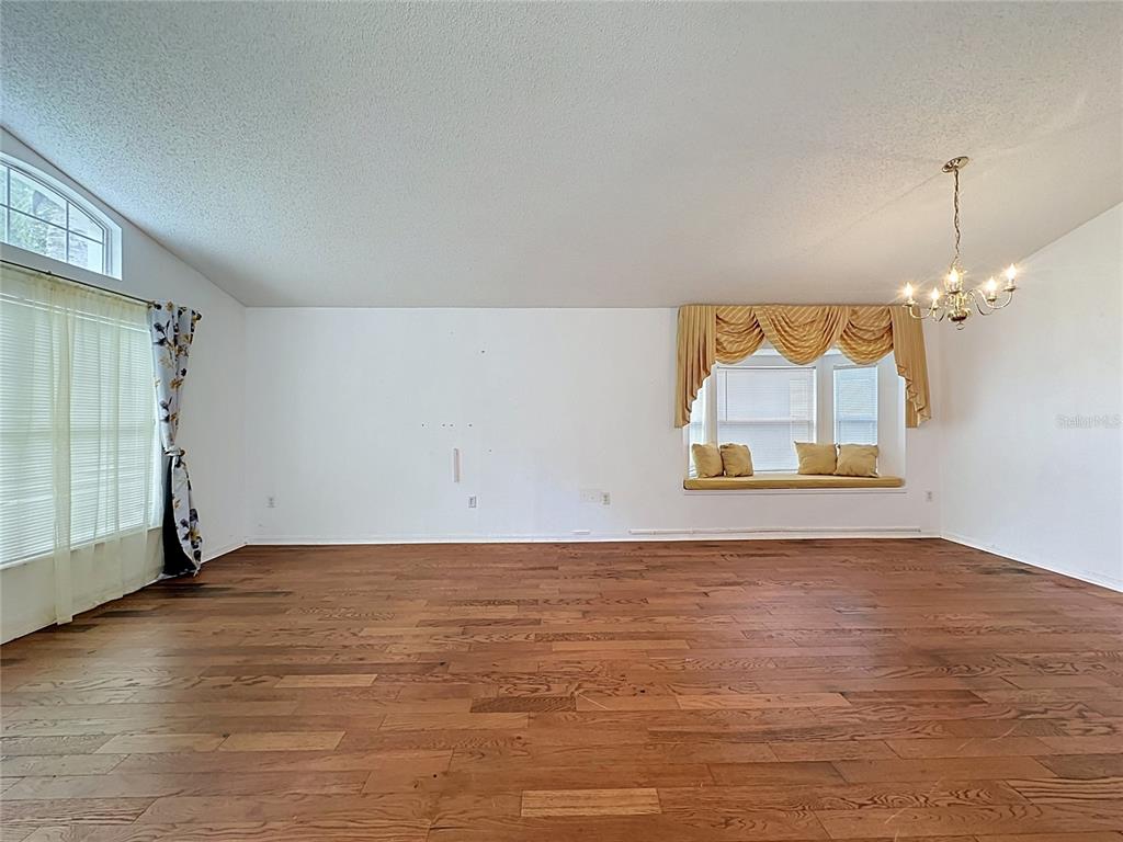 An empty room features hardwood flooring, a window seat with gold valance, and a chandelier — 3122 MONTSERRAT WAY, HAINES CITY, FL