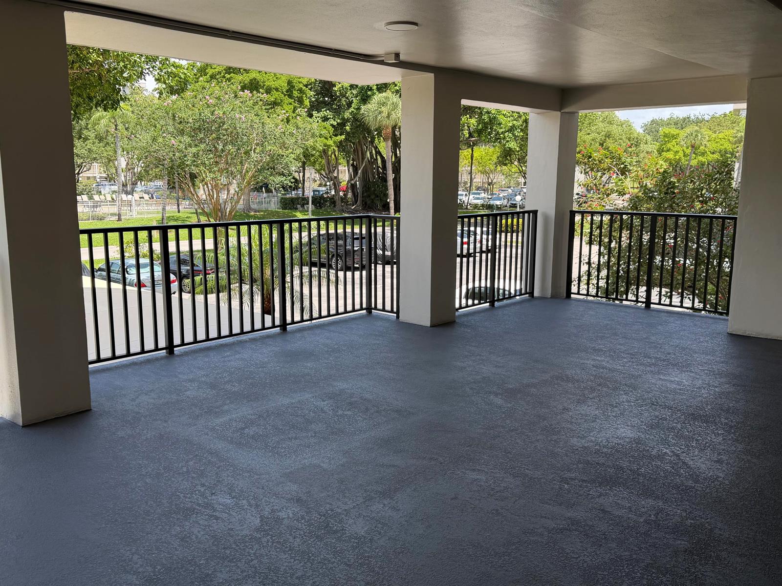 A covered balcony with dark gray flooring and black metal railings overlooks a parking lot — 2650 S Course Drive # 203, Pompano Beach FL 33069, POMPANO BEACH, FL