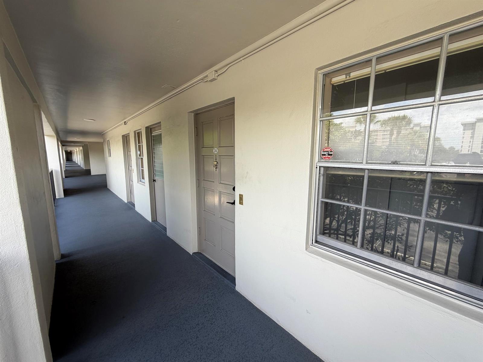 An exterior apartment hallway features a row of doors and windows along a concrete walkway — 2650 S Course Drive # 203, Pompano Beach FL 33069, POMPANO BEACH, FL