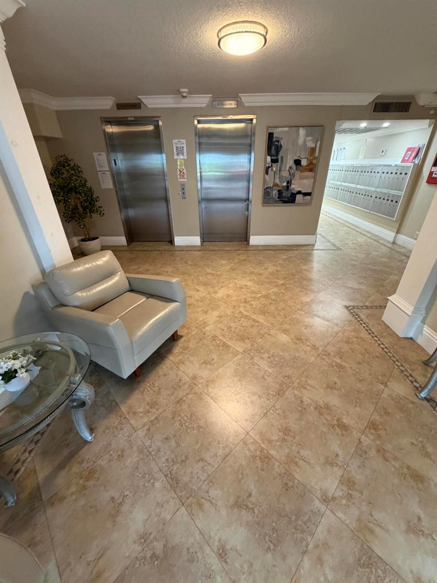 A lobby area features two elevators, a leather armchair, a glass table, and wall-mounted mailboxes — 2650 S Course Drive # 203, Pompano Beach FL 33069, POMPANO BEACH, FL