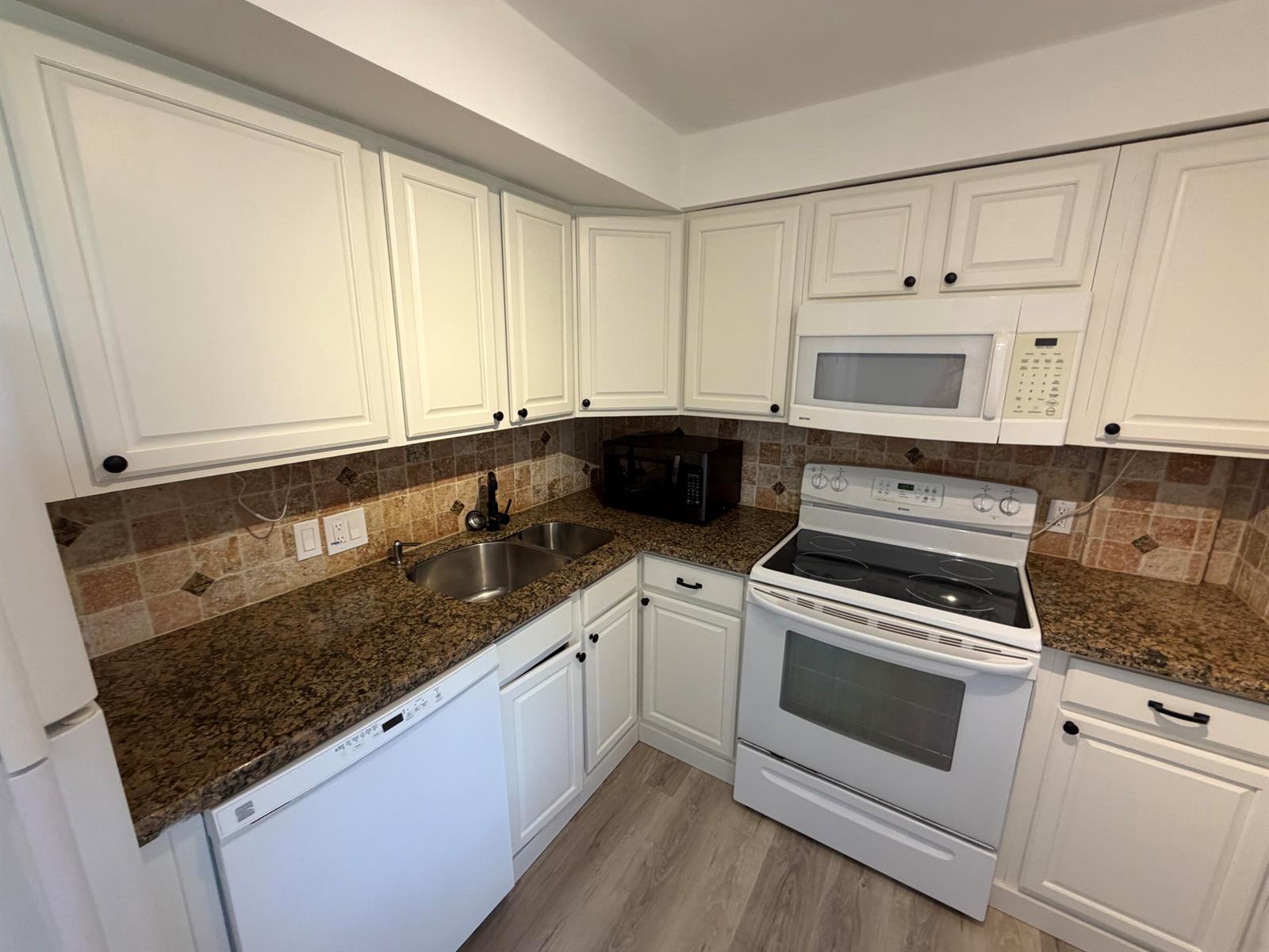 A kitchen features white cabinets, granite countertops, a double sink, and white appliances — 2650 S Course Drive # 203, Pompano Beach FL 33069, POMPANO BEACH, FL