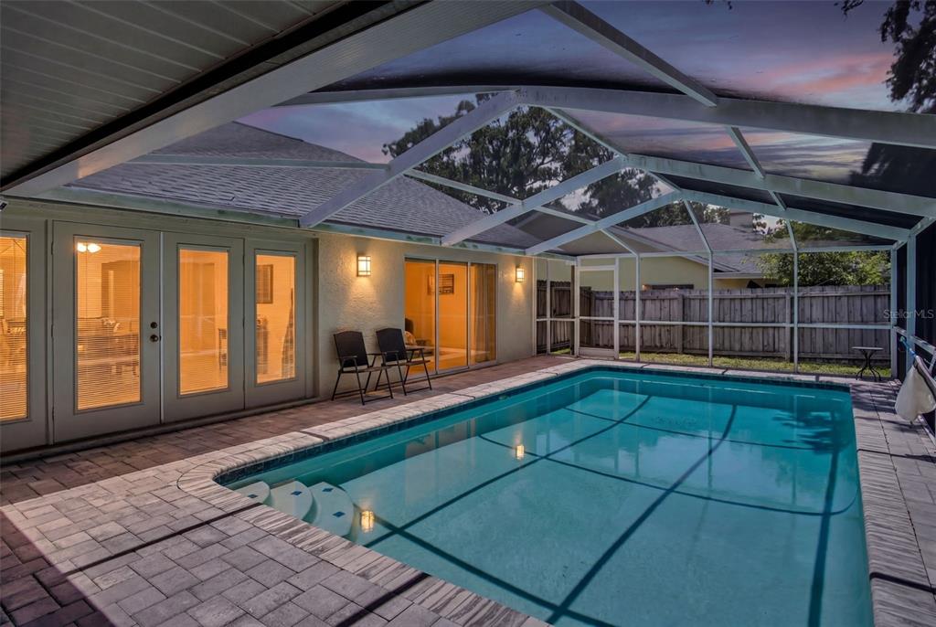 A screened-in swimming pool with a brick paver deck sits behind a house at dusk — 2654 CRYSTAL CIRCLE, DUNEDIN, FL