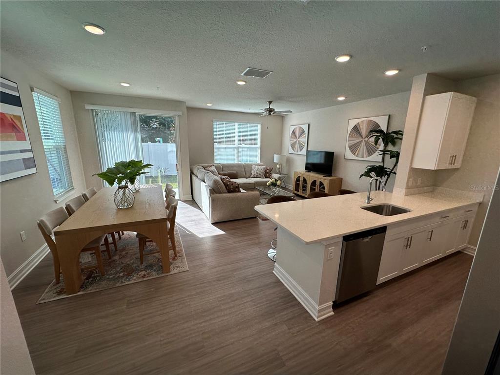 An open-concept kitchen, dining area, and living room featuring light wood flooring and white cabinetry — 1129 E CAROLINE STREET, TAVARES, FL
